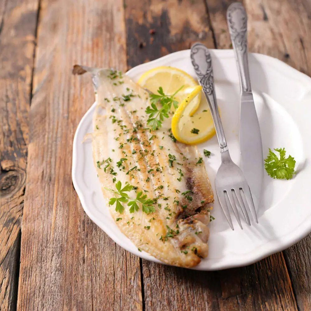 Serveringsförslag: smörstekt fisk med citron och persilja på träbord